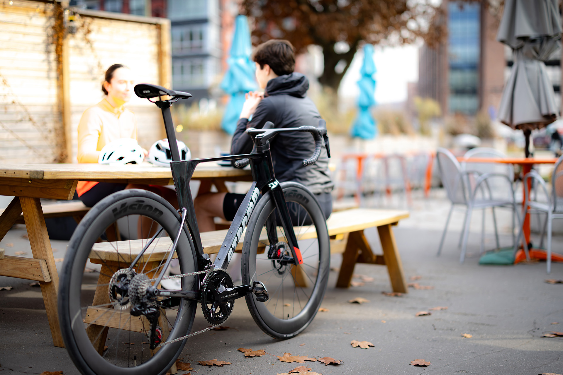 A black Stromm road bike leaning against an outdoor cafe bench while the rider enjoys lunch.